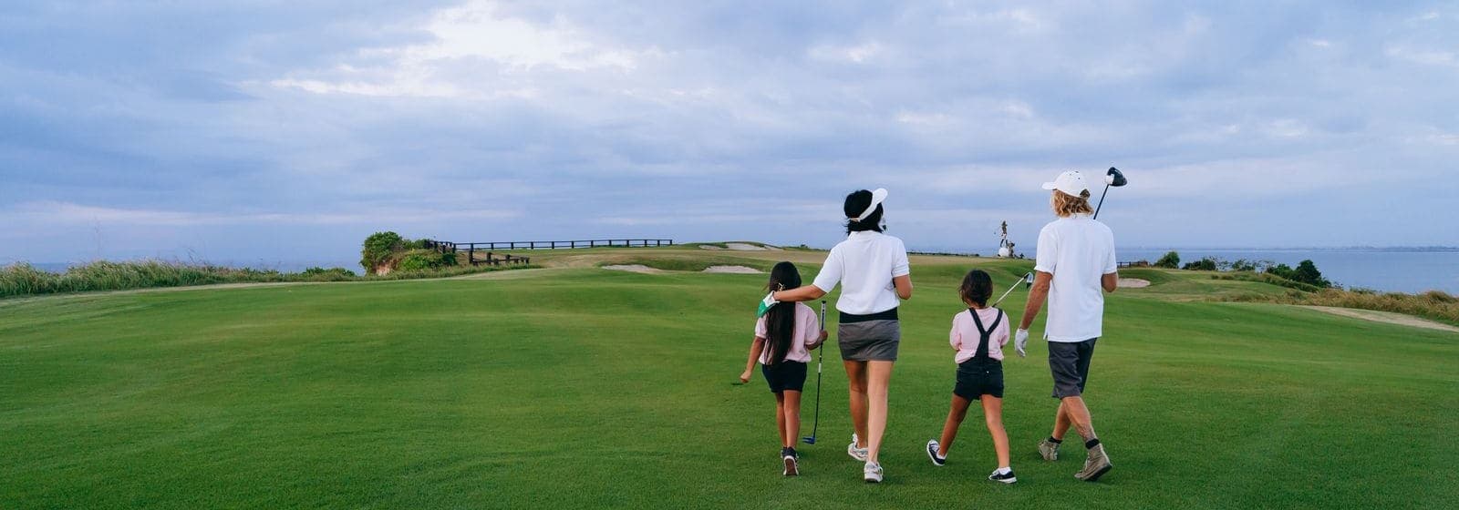 A family walking together down a golf fairway toward the sea under a cloudy sky