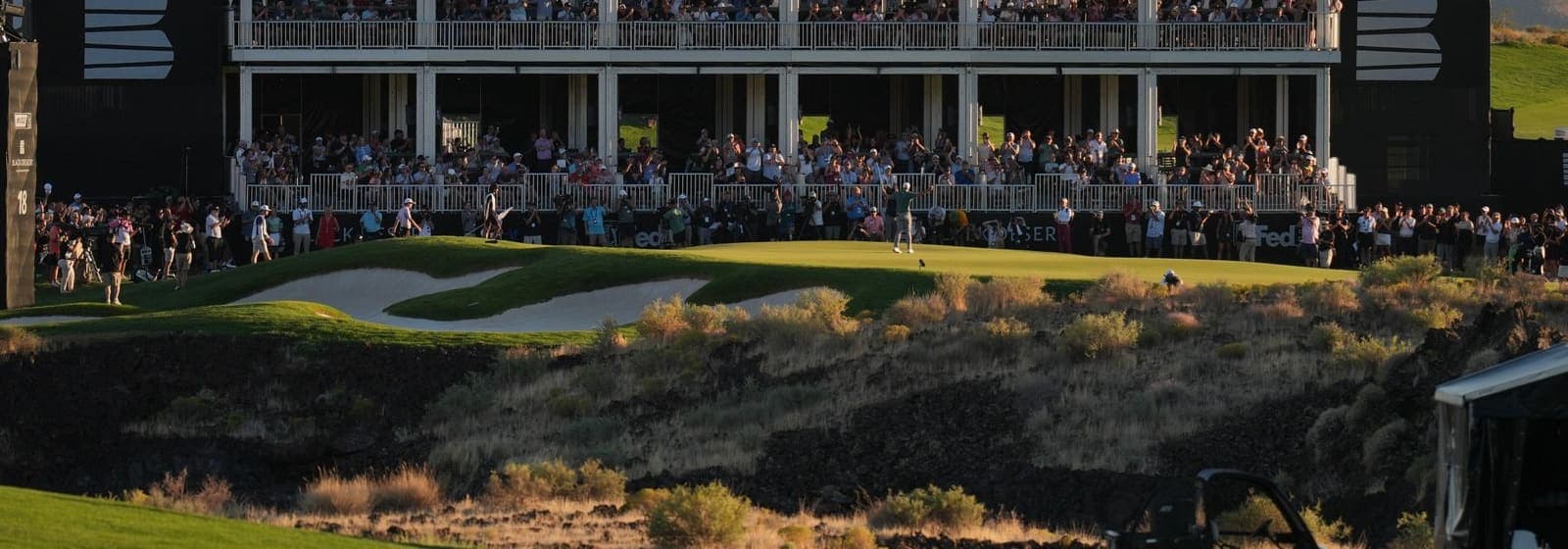 A large crowd watching from a grandstand beside the green at a professional golf event