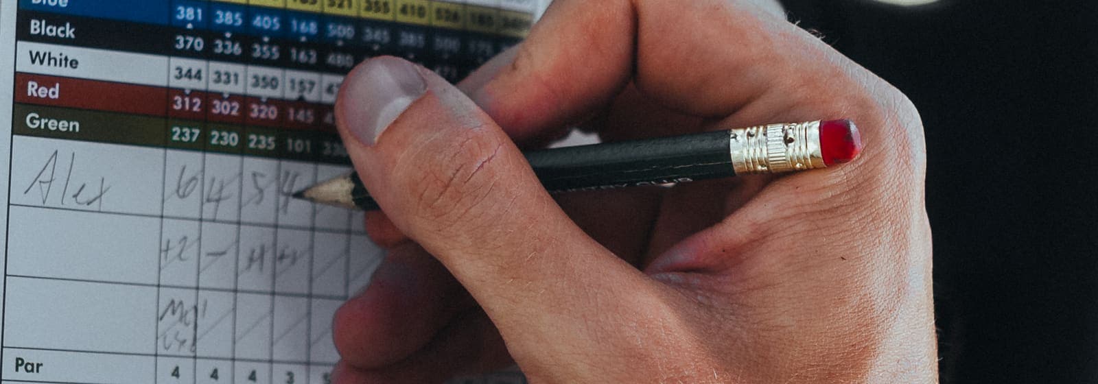 A hand writing on a golf scorecard with a pencil