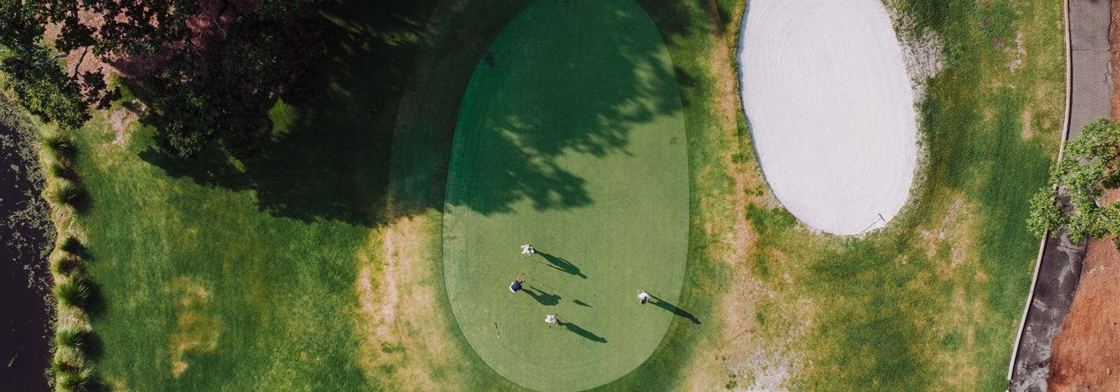 Aerial view of a golf green with three golfers, surrounded by bunkers and trees