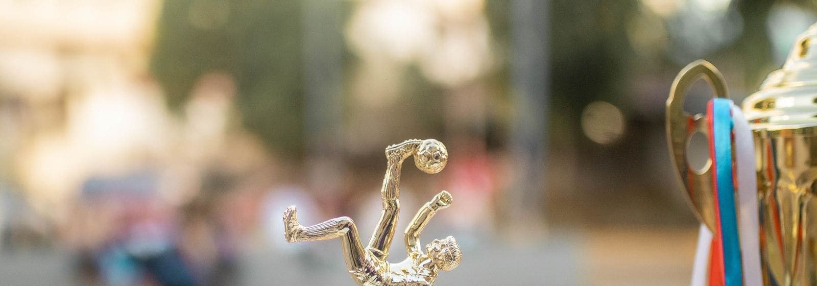 A golden soccer trophy with colored ribbons beside a small player figurine