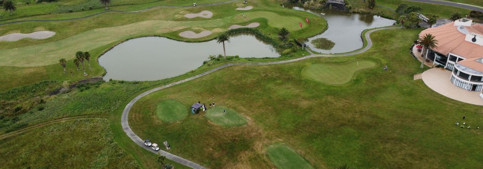 Aerial view of a golf course with a lake, winding cart paths, and a clubhouse